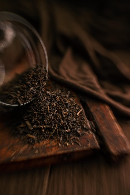 El té secado con hojas se vierte de un frasco de vidrio sobre una mesa marrón de madera sobre un fondo oscuro con un efecto bokeh