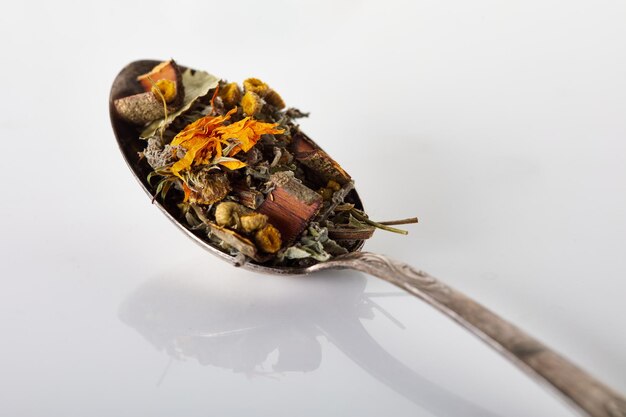 Foto el té seco de hierbas, flores, bayas, semillas y corteza se vierte en una cuchara de metal plateado en una mesa gris con una superficie brillante