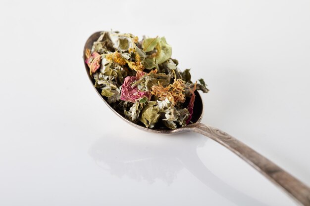 Foto el té seco de hierbas, flores, bayas, semillas y corteza se vierte en una cuchara de metal plateado en una mesa gris con una superficie brillante