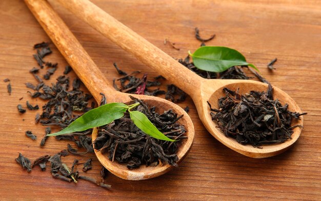 Té seco con hojas verdes en cucharas de madera sobre fondo de madera