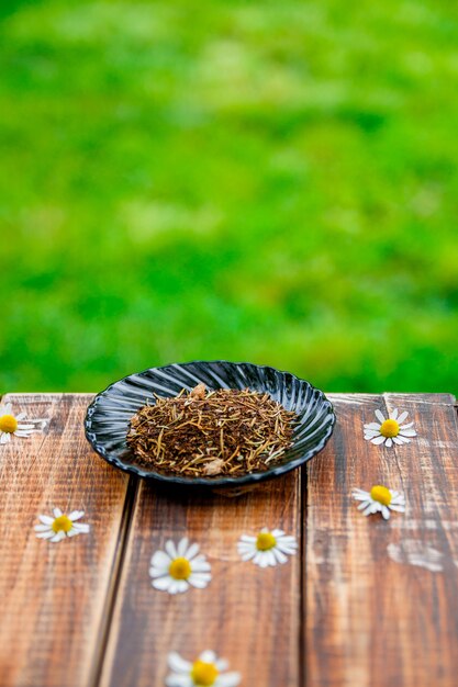 Té seco en placa en mesa de madera con flores de manzanilla jardín y en la naturaleza. té . hojas de té. de cerca