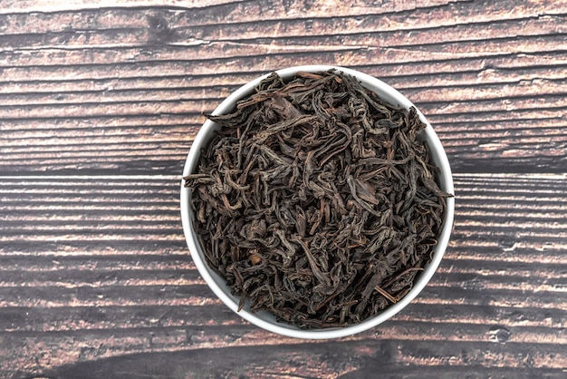 El té seco se vierte en una taza de cerámica sobre una mesa de tablones de madera. Vista desde arriba.