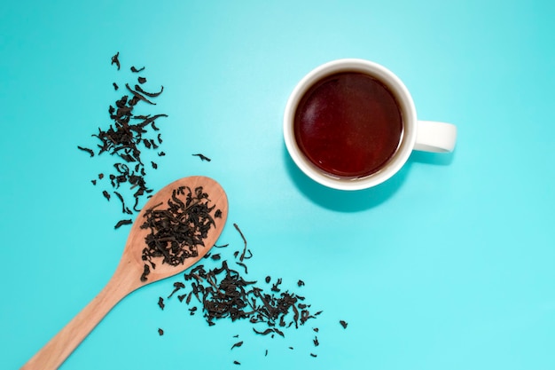 Té en una taza blanca, una cuchara de madera, esparcido con té de hojas a medio pecho sobre un azul turquesa