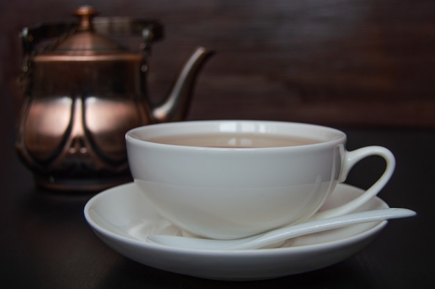 Té en taza blanca con platillo y tetera sobre un fondo oscuro