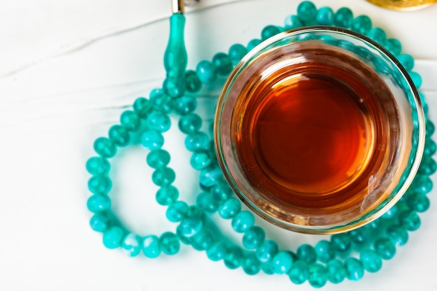 Té en taza de cristal y rezar perlas sobre fondo blanco.