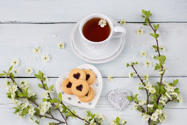 Té en una taza, galletas y ramas de cerezo sobre la mesa