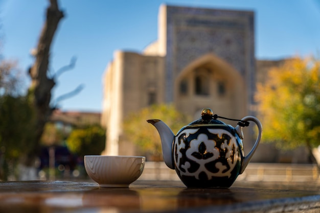 Té en taza de porcelana de tradición oriental y tetera en el contexto de una hermosa arquitectura de madraza en el estilo medieval de Asia Central