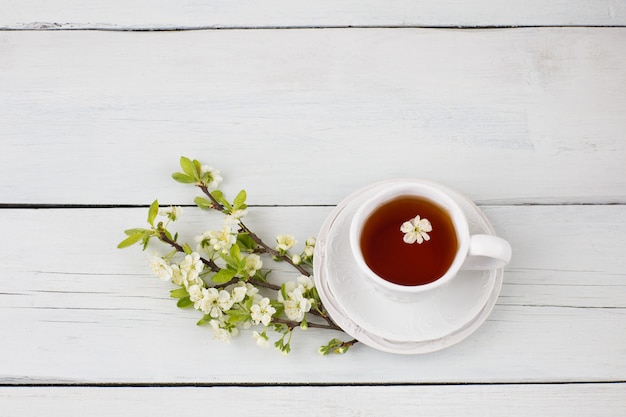 té en una taza y ramas de cerezo sobre la mesa