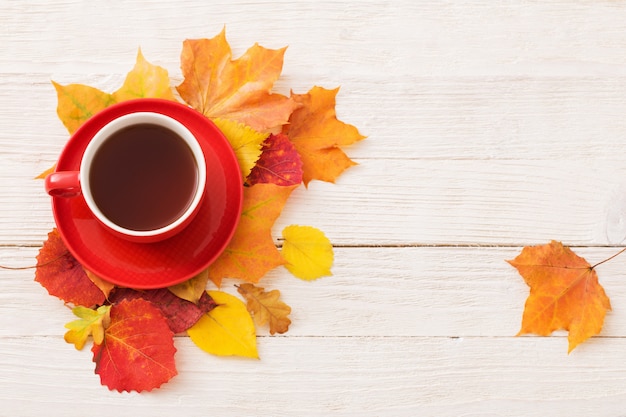 Té en taza roja con hojas de otoño en mesa blanca