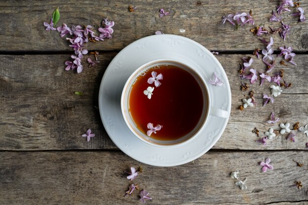 Té en taza de té blanco, pétalos de flores lilas en la mesa de madera vieja