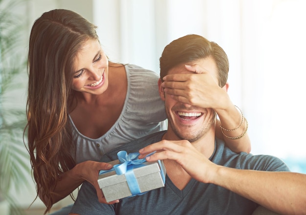 Te tengo algo cariño Una mujer joven que cubre los ojos de su marido para un regalo sorpresa