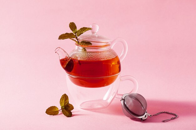 Té en una tetera de vidrio sobre un fondo rosa y un Filtro Infusor de metal