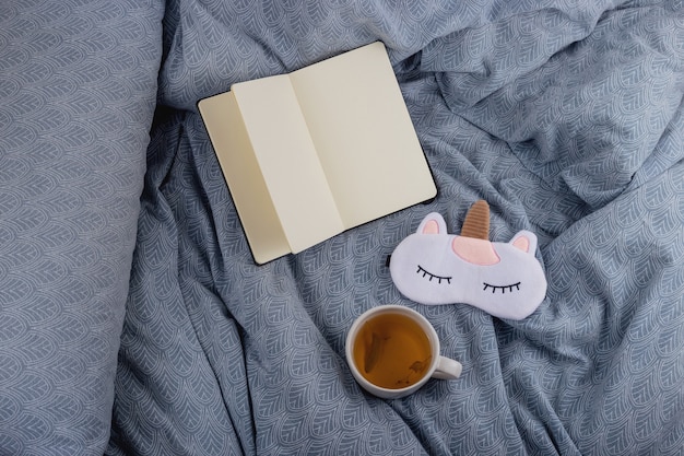 Té de tilo para un sueño saludable en la cama junto a un libro y una máscara para dormir