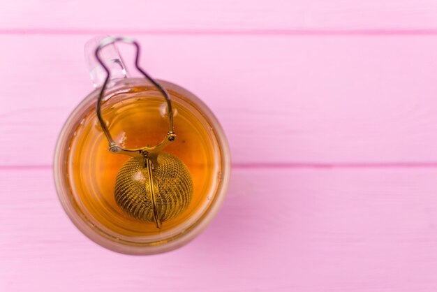 Té en un vaso con una cucharadita sobre un fondo de madera rosa