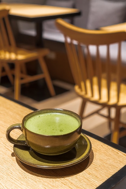 El té verde caliente contiene una taza de color oscuro con un plato pequeño colocado sobre una mesa de madera con ambiente de café