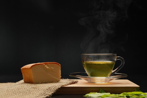 Foto el té verde caliente en la taza de vidrio con pastel de mantequilla y humo sobre la tabla de madera.