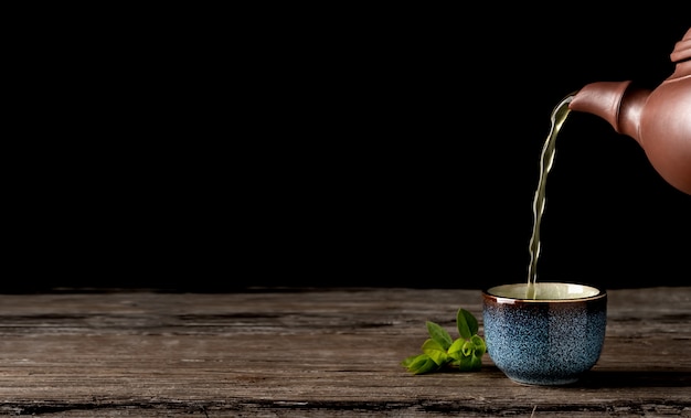 El té verde caliente se vierte de la tetera en el recipiente azul