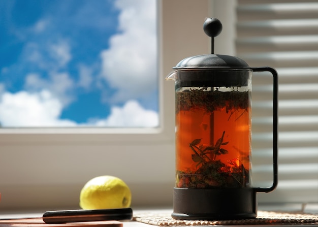 Té verde exótico con flores en tetera de vidrio en la ventana