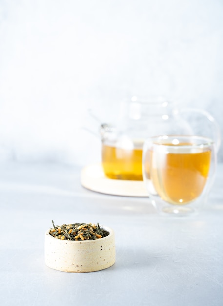 Té verde japonés Genmaicha. Hojas de té con arroz integral frito sobre un fondo gris brillante con una sombra. Concepto de té de tendencia adelgazante. una taza de té. preparar una tetera transparente