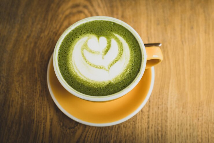 té verde matcha latte con espuma muy densa y un hermoso patrón en una taza amarilla sobre una mesa de madera
