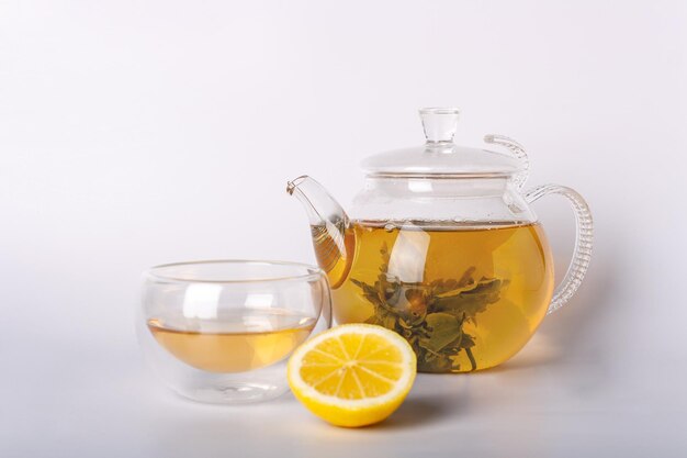 Té verde en vaso de vidrio y tetera y limón sobre fondo blanco.