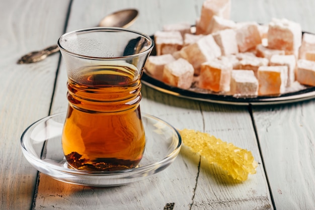 Té en vidrio árabe con delicias turcas Rahat Lokum sobre superficie de madera