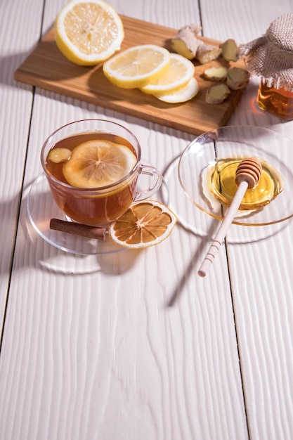 Té de vitamina en una taza de vidrio con miel de limón y jengibre sobre un fondo blanco de tablero de corte de madera