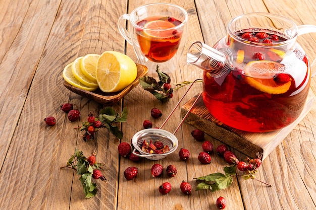 Té vitamínico caliente con escaramujos sobre un podio de madera y una mesa con una taza de té y rodajas de limón fitoterapia bebidas antifrío