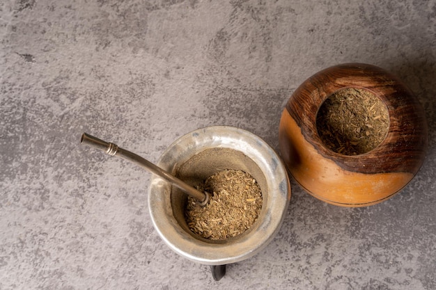 Foto té de yerba mate junto a una calabaza llena de yerba mate sobre un fondo gris claro