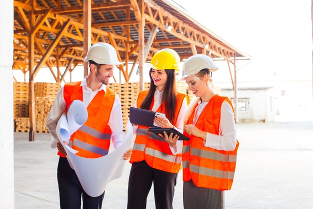 Team junger Architekten, die Tablette und Blaupausen auf Konstruktionen verwenden