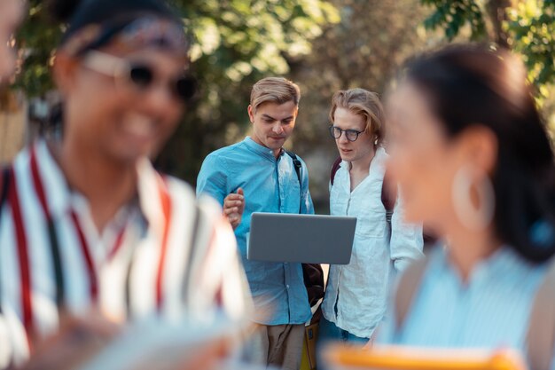 Team-Projekt. Zwei konzentrierte Studenten stehen hinter ihren Mitschülern und arbeiten am Laptop außerhalb der Universität an ihrem Projekt.