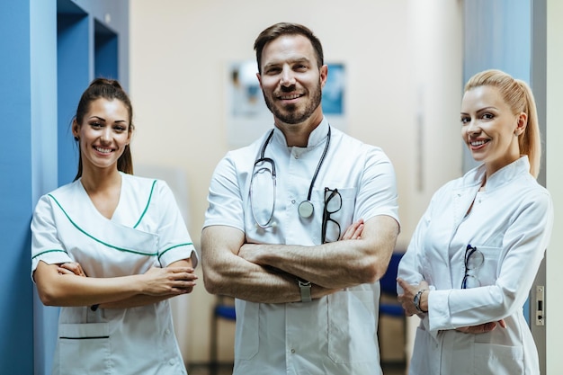 Team selbstbewusster Ärzte, die mit verschränkten Armen in der medizinischen Klinik stehen und in die Kamera schauen