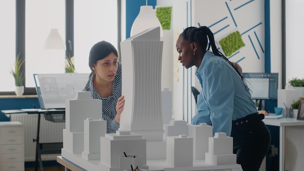 Team verschiedener Frauen, die mit dem Baumodell zusammenarbeiten, um das Baulayout zu entwerfen. Junge Architekten verwenden Maquette, um an Stadtentwicklungsprojekten zu arbeiten und Ideen zu sammeln.