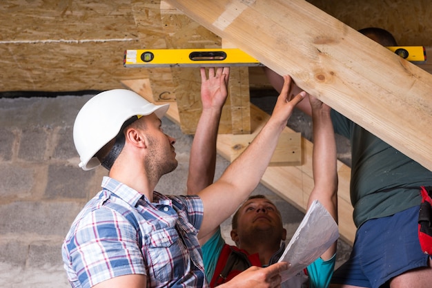 Team von Bauarbeitern, die Holztreppen bauen, die Ebenen auf Genauigkeit und Qualitätskontrolle im unfertigen Keller des neuen Hauses überprüfen