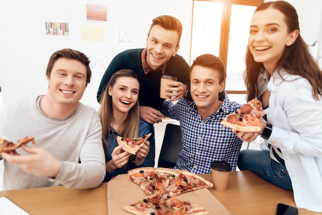 Team von den jungen glücklichen Menschen, die Pizza an der Mittagspause essen