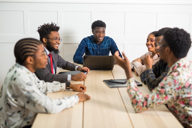 Team von jungen afrikanischen Leuten, die im Büro am Tisch mit Laptop arbeiten