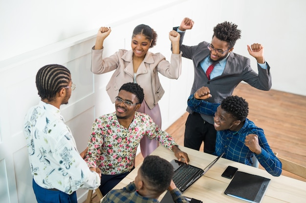 Team von jungen afrikanischen Leuten, die im Büro am Tisch mit Laptop arbeiten