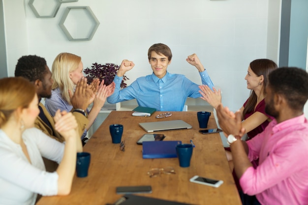 Team von jungen schönen Menschen im Büro mit den Händen nach oben