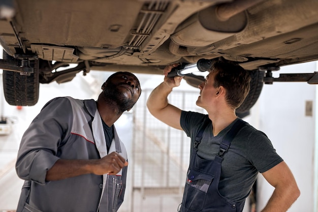 Team von verschiedenen Automechanikern, die am Fahrwerk der Auto-Fleiß-Aufmerksamkeits-Inspektionsprüfung arbeiten ...