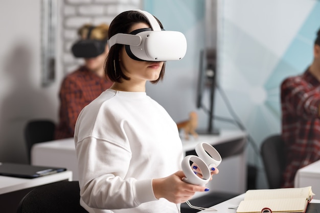 Team von vier kreativen Ingenieuren, die mit virtueller Realität arbeiten, junge Frau, die VR-Brillen oder Schutzbrillen testet, die im Büroraum sitzen