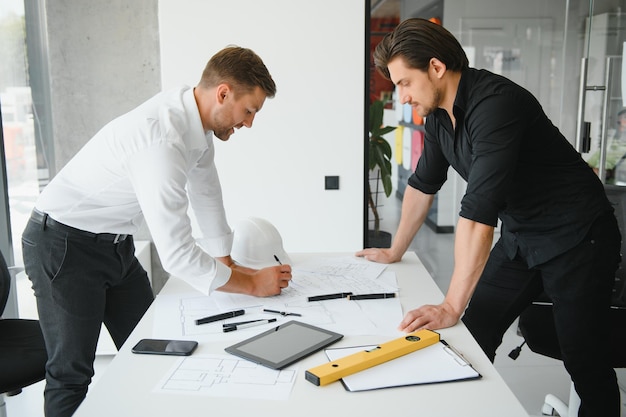 Teamarbeit von Ingenieuren oder Architekten, die an Bauprojekten mit Gebäudemodell und Blaupause im Büro arbeiten Baukonzept