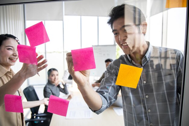 Teamwork-Konzept von Geschäftsleuten, die sich im Büro mit der Verwendung von Notizen auf einer klaren Tafel treffen, um Ideen bei der Arbeit im Besprechungsraum zu teilen. Konferenz, um den Fortschritt der Organisation zu analysieren und zu ermitteln.