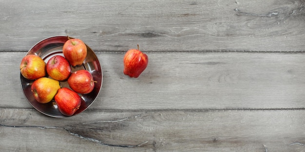 Teble top view (largo, lado direito é espaço para texto) de maçãs vermelhas maduras brilhantes em tigela de metal, colocadas na mesa de madeira cinza.