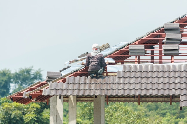 Techador de construcción instalando tejas en el sitio de construcción de viviendas