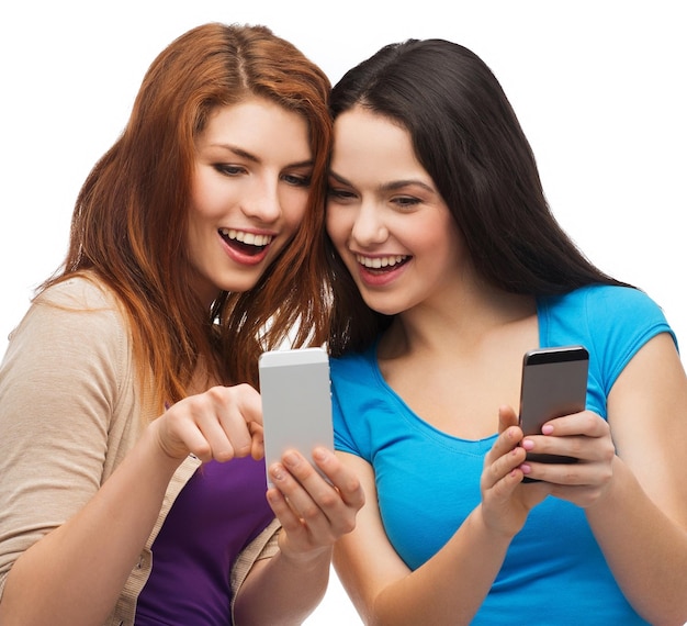 Technologie-, Freundschafts- und Menschenkonzept - zwei lächelnde Teenager, die mit dem Finger auf den Smartphone-Bildschirm zeigen