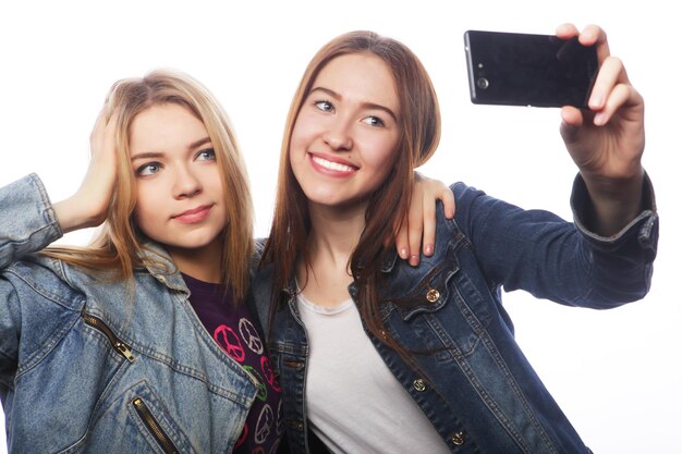 Technologie-, Freundschafts- und Menschenkonzept - zwei lächelnde Teenager, die mit Smartphone-Kamera fotografieren