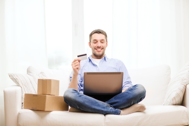 Technologie-, Heim- und Lifestyle-Konzept - lächelnder Mann mit Laptop, Kreditkarte und Kartons zu Hause
