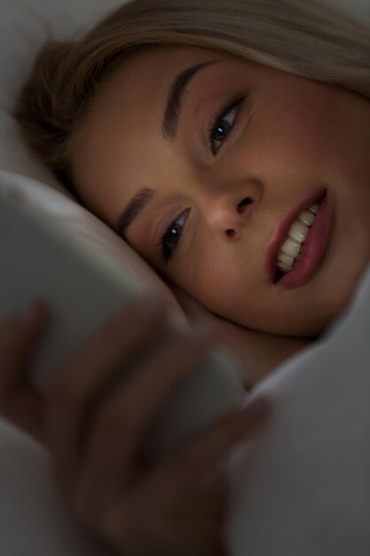 technologie-, internet-, kommunikations- und personenkonzept - glücklich lächelnde junge frau, die nachts auf dem smartphone im schlafzimmer zu hause eine sms schreibt