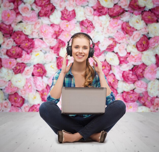 Technologie-, Internet- und People-Konzept - lächelnde junge Frau in lässiger Kleidung, die mit Laptop-Computer und Kopfhörern auf dem Boden liegt