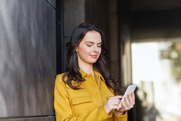 technologie-, kommunikations- und menschenkonzept - lächelnde junge frau oder mädchen, die auf dem smartphone auf der stadtstraße sms schreiben